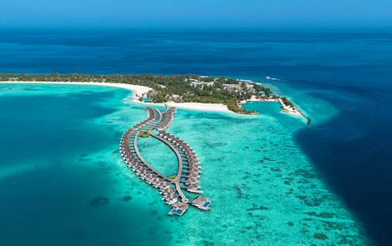 Aerial view of overwater bungalows arranged in a unique shape over a turquoise lagoon with coral reefs and a tropical island with white sandy beaches in Kudahuvadhoo Dhaalu Atoll Maldives. Aerial view of overwater bungalows arranged in a unique shape over a turquoise lagoon with coral reefs and a tropical island with white sandy beaches in Kudahuvadhoo Dhaalu Atoll Maldives.