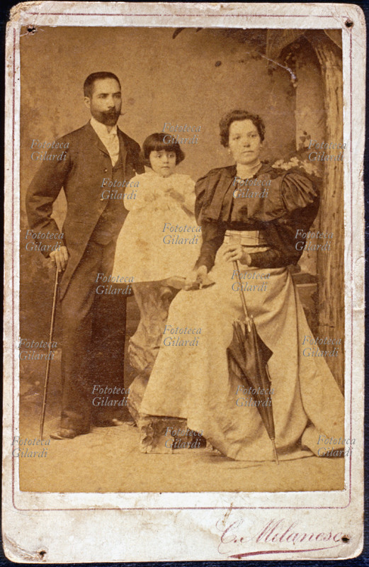FAMIGLIA genitori e figlioletta in posa dal fotografo alla moda. Fotografia di C. Milanese, formato gabinetto. Italia, 1895 circa.