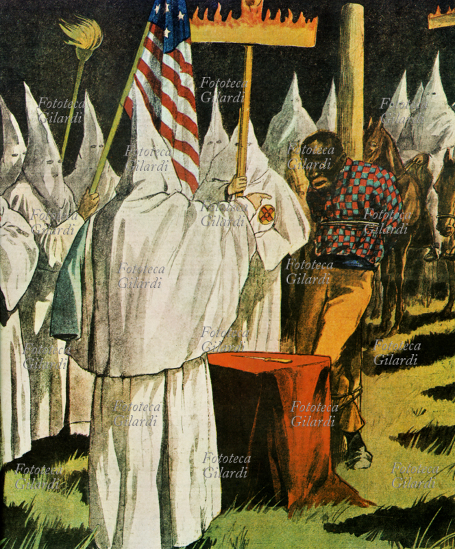 RACISM A black man, represented with a physiognomy stereotyped and caricatured, with round pink lips, is tied to a pole and tortured by members of the Ku Klux Klan at a rally of the cruel racist sect. Popular press of 1923.