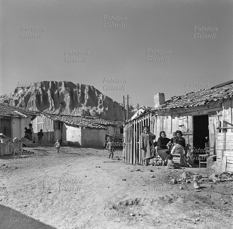 FAMIGLIA madre pettina la figlia dinnanzi alla porta di casa. Accanto a loro, sorridenti, altri parenti e l\