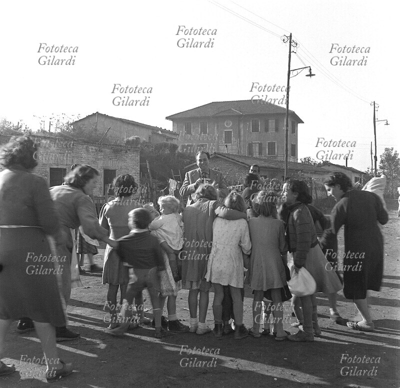 Ando GILARDI (8 giugno 1921 – 5 marzo 2012), divertito, fotografato mentre a sua volta riprende con un apparecchio di piccolo formato un vivace gruppo di bambini in \