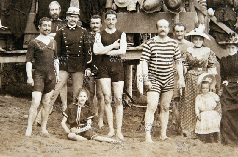 MARE gruppo di bagnanti e personale dei bagni, in costume da bagno o in abiti estivi, in spiaggia (dettaglio da gruppo più esteso #13024). Fotografia viraggio seppia, Savona 1905 circa