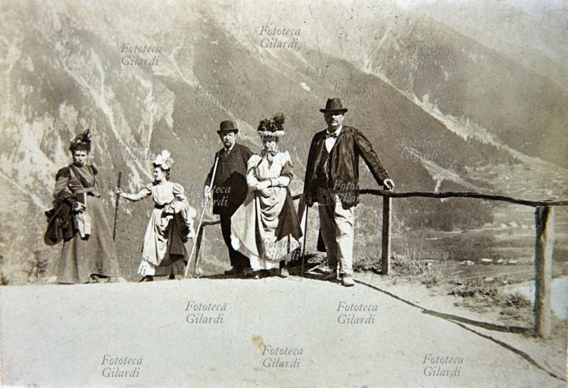 MONTAGNA gruppo di turisti, tre donne e due uomini, in posa durante la pausa di una escursione in montagna: suggestivo lo sfondo panoramico roccioso. Fotografia amatoriale, viraggio seppia, Italia 1895 circa.