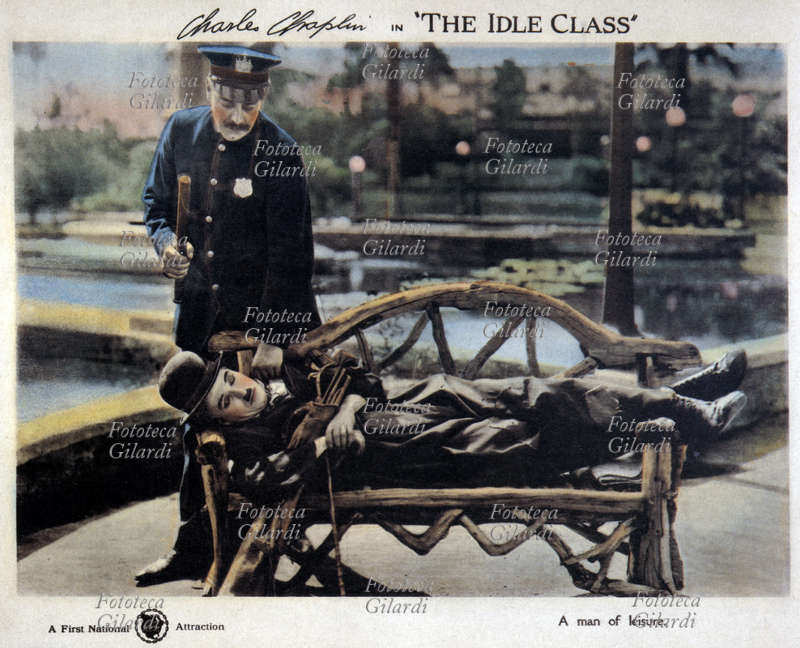 CINEMA Locandina per il film "Ricchi e vagabondi" (titolo originale "The Idle Class") scritto, diretto ed interpretato da Charles Chaplin, basato sugli equivoci scaturiti dal fortuito incontro di un ricco dissipato e il suo sosia vagabondo. Nella foto il vagabondo è sorpreso a dormire su una panchina da un poliziotto che lo minaccia con lo sfollagente. Stati Uniti d\