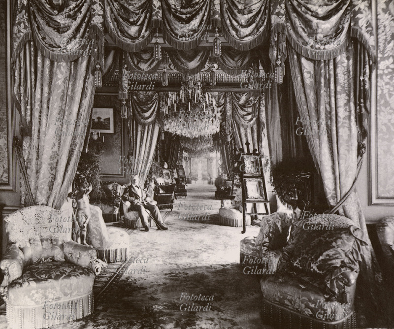 FURNISHINGS Entrance hall of Cliffe Castle in Yorkshire, owned by industrialist Henry Isaac Butterfield. In the sumptuous perspective, accentuated by the draperies, the man sitting in one of the innumerable armchairs passes almost unnoticed; some paintings are housed on easels in front of the windows, to be better appreciated in the daylight, rather than illuminated by the imposing chandeliers. United Kingdom, circa 1880.