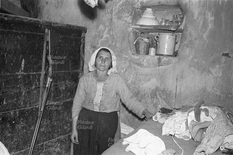 ALBANO DI LUCANIA Donna ritratta nella sua casa davanti ad uno scaffale con le povere stoviglie per mangiare. La figlia era afflitta da assalti violenti di natura apparentemente paranormale e non acconsentì a farsi fotografare se non in chiesa (v. 10296). Immagine a documentazione dell\