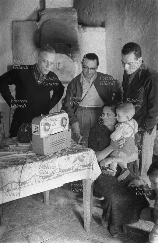 SUD E MAGIA Ernesto De Martino (1º dicembre 1908 – 9 maggio 1965), etnologo e antropologo ed i professori Emilio Servadio (14 agosto 1904 – 18 gennaio 1995), esoterista, parapsicologo e giornalista, e Romano Calisi (4 maggio 1931 - 20 maggio 1975) antropologo ed esperto di mezzi di comunicazione di massa, ascoltano la registrazione del racconto di un episodio di magia insieme alla protagonista, seduta con in braccio il bambino. Immagine a documentazione dell\