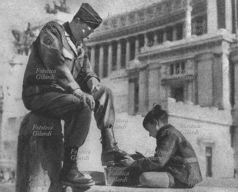 II GM ITALIA Uno "sciuscià" lustra le scarpe a un soldato americano in Piazza Venezia, subito dopo la Liberazione. Roma, giugno 1944.