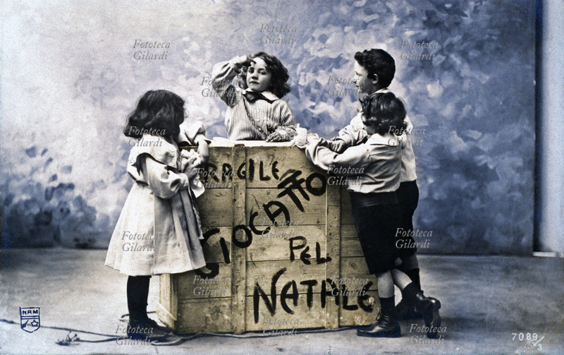 NATALE quattro bambini intorno ad una cassa di legno con la scritta: "Fragile, giocattoli pel Natale". Fotografia, Torino 1905.