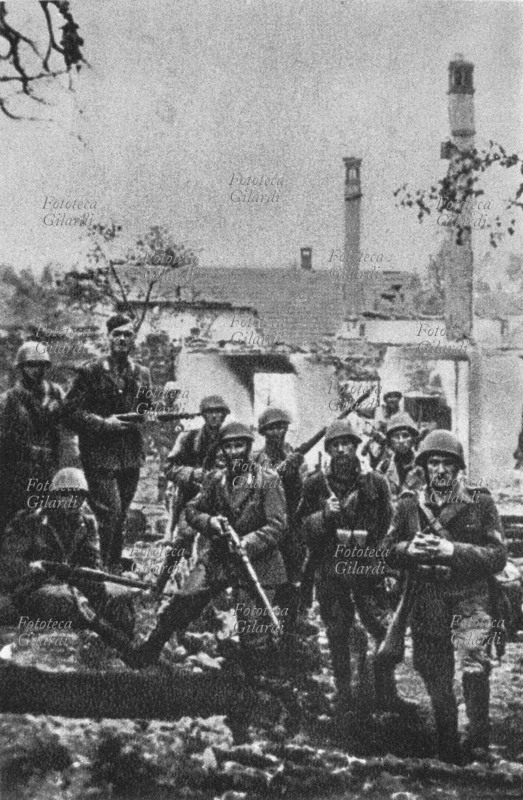 II GUERRA MONDIALE Gruppo di soldati italiani posano per una foto ricordo, davanti alle case di un villaggio incendiato e saccheggiato. Fotografia spontanea, Jugoslavia 1942