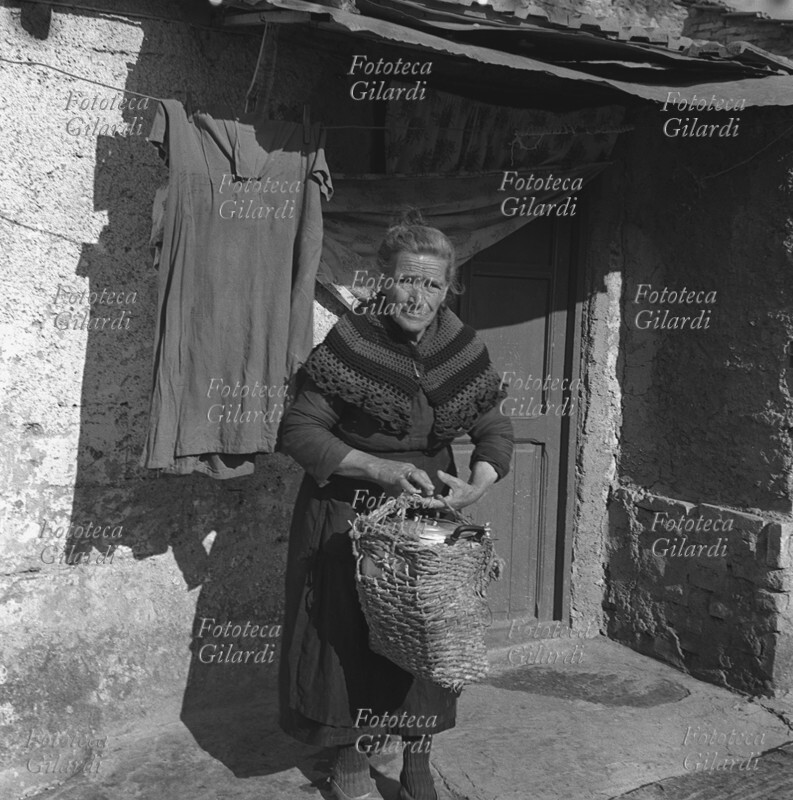 DONNA anziana trasporta pasti caldi in una pentola, con una vecchia borsa di paglia sdrucita; abitante di \
