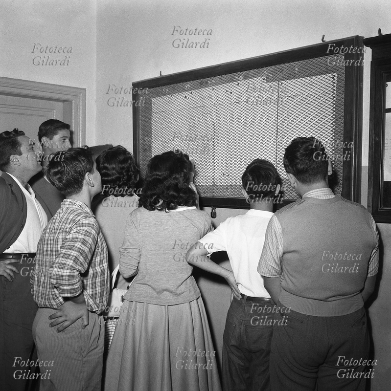 SCUOLA Studenti del liceo Scientifico Augusto Righi, di spalle al fotografo, leggono i tabelloni con le valutazioni. Fotografia di Ando Gilardi (1921 - 2012), #andogilardi, Roma circa 1952.