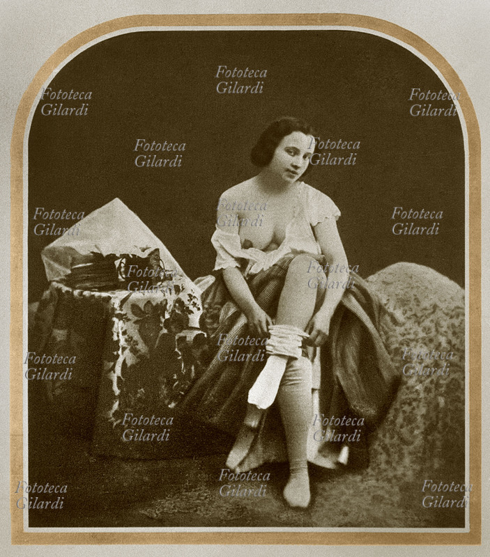 EROTISMO giovane donna in camera, fotografata sul letto mentre si toglie le calze. Francia 1850