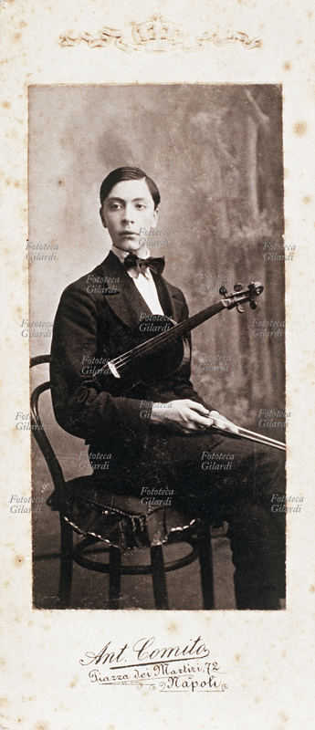 MUSICA Giovane violinista posa per una fotografia, seduto con lo strumento sottobraccio. Indossa l\