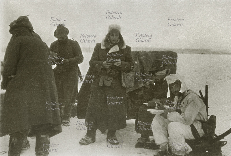 II G.M. URSS ITALIA 1943 Alpini durante la ritirata, durante un momento di riposo in una breve sosta. Due mangiano una minestra seduti sulla slitta, gli altri tre sostano in piedi. Rara testimonianza fotografica di Gianfranco Ucelli (Divisione Julia, Battaglione Aquila, 3° Art. Alpini.) reduce sopravvissuto alla tragica spedizione in Russia. Fotografia, 1943.