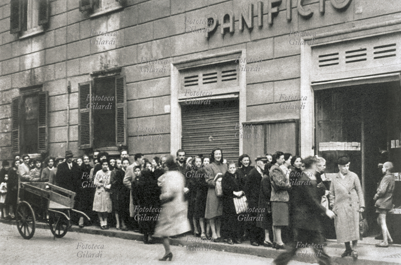 II G.M. ITALIA una piccola folla in rassegnata attesa, la coda per il pane davanti ad un esercizio che distribuisce le razioni alle famiglie su presentazione delle tessere annonarie, Roma 1941