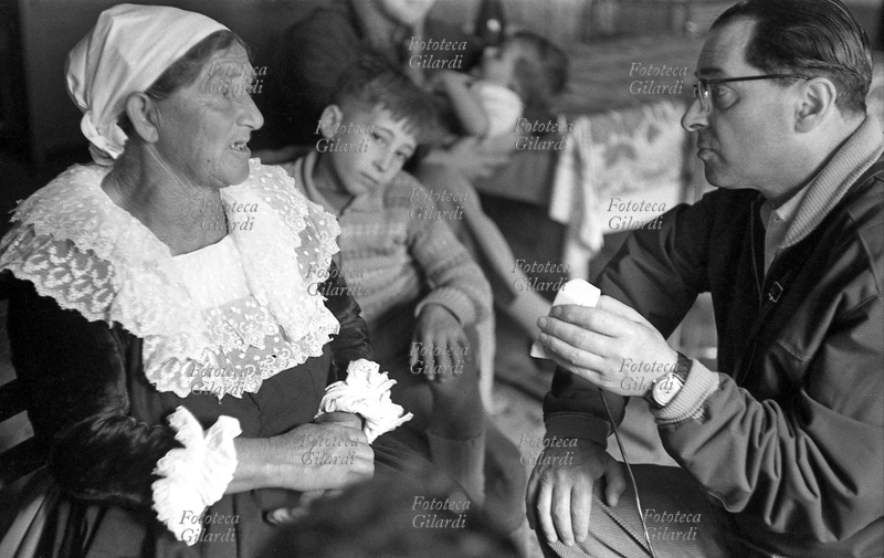 COSTANTINO ALBANESE Donna in abiti tradizionali intervistata da Emilio Servadio (14 agosto 1904 - 18 gennaio 1995, psicoanalista, parapsicologo, esoterista e giornalista), membro della squadra diretta da Ernesto De Martino (1º dicembre 1908 - 9 maggio 1965, etnologo, antropologo, storico delle religioni e filosofo) che dal 15 maggio al 4 giugno 1957 ha condotto una spedizione antropologica in Lucania, descritta da De Martino nel libro \