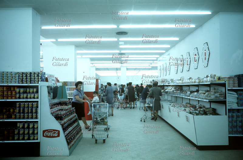 SUPERMERCATO Interno di un supermercato, reparto dolci. La corsia è impegnata prevalentemente da donne che spingono i carrelli della spesa, una ha fatto sedere il bambino nell\