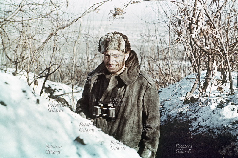 SECONDA GUERRA MONDIALE Roberto Cacchi (1914-2004), tenente alpino di vedetta in prima linea, ritratto sorridente con il binocolo al collo. Il tenente, autore di rare testimonianze fotografiche a colori della tragica spedizione in Russia, aveva chiesto all\