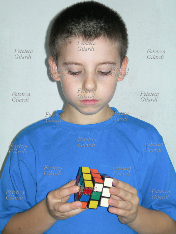 GIOCHI un bambino cerca di risolvere il Cubo di Rubik. Il Cubo di Rubik è un gioco rompicapo inventato dal professore di architettura e scultore ungherese Ernö Rubik nel 1974. Lo scopo del gioco è di risalire alla posizione originale dei 26 cubetti portando il cubo ad avere per ogni faccia un colore uguale. Il cubo può assumere ben 43.252.003.274.489.856.000 combinazioni diverse, solo una delle quali è quella corretta. Il gioco divenne molto diffuso e popolare, la stima delle vendite nel 1982 superava i 100 milioni di pezzi.