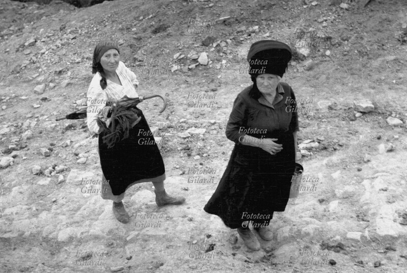 DONNE in cammino, incontrate nella campagna lucana. La più giovane di loro porta un ombrello sotto braccio, l\