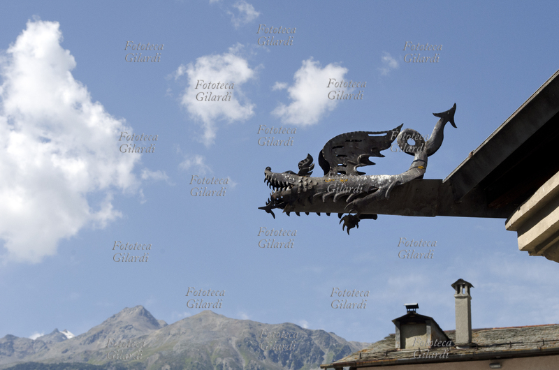 DRAGO doccione a forma di drago in ferro battuto, decorazione del pluviale del tetto del Kuerc (in dialetto bormino coperchio, copertura) di Piazza Cavour, una tettoia in pianta trapezoidale risalente al XIV secolo, sotto la quale sono collocate delle panche a semicerchio, luogo della collettività in cui anticamente avvenivano le adunanze pubbliche e si amministrava la giustizia. Fotografia di Elena Piccini, Bormio (Sondrio), agosto 2017