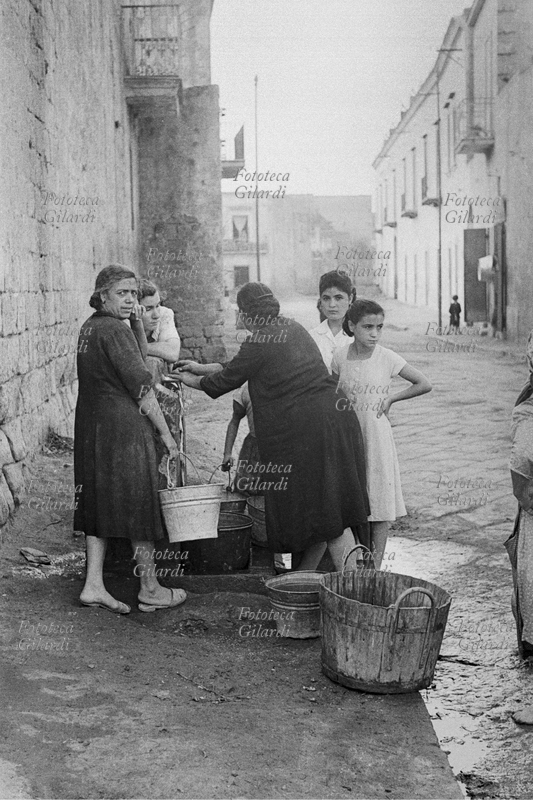 QUALIANO Donne e ragazze alla fontana, fanno provvista di acqua e si scambiano informazioni e notizie aspettando che si riempiano i secchi. Fotografia di Ando Gilardi (1921 - 2012) #andogilardi da una serie realizzata per \