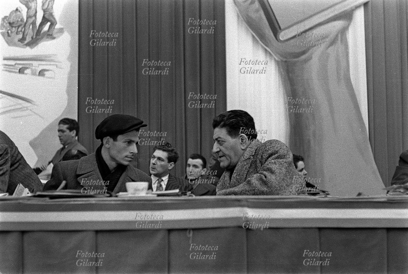 Giuseppe DI VITTORIO (1892-1957) sul palco discorre con il figlio di Paolo Vitale, bracciante di Comiso ucciso dalla polizia; seduto accanto a lui, Di Vittorio è di tre quarti (vedi anche 45726, 5955 e 5957). Sulla fila dietro, tra loro, si vede seduto un giovane Luciano Lama (14 ottobre 1921 – 31 maggio 1996). 4° Congresso CGIL, cinquantenario della fondazione. Fotografia di Ando Gilardi (1921 - 2012) #andogilardi, Roma EUR, 1956.