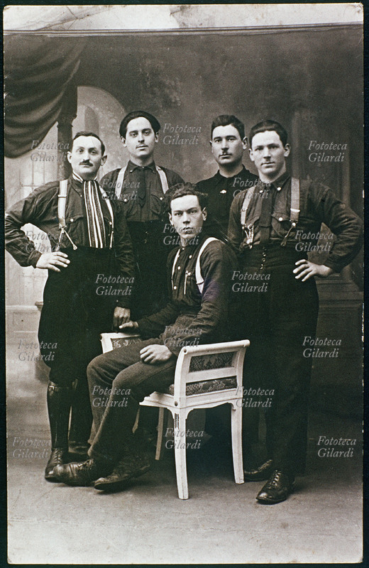 GRUPPO MASCHILE Gruppo di cinque giovani in posa per una fotografia ricordo. Quello al centro è seduto su una poltroncina, tutti indossano pantaloni e camicia nera. Italia, 1925