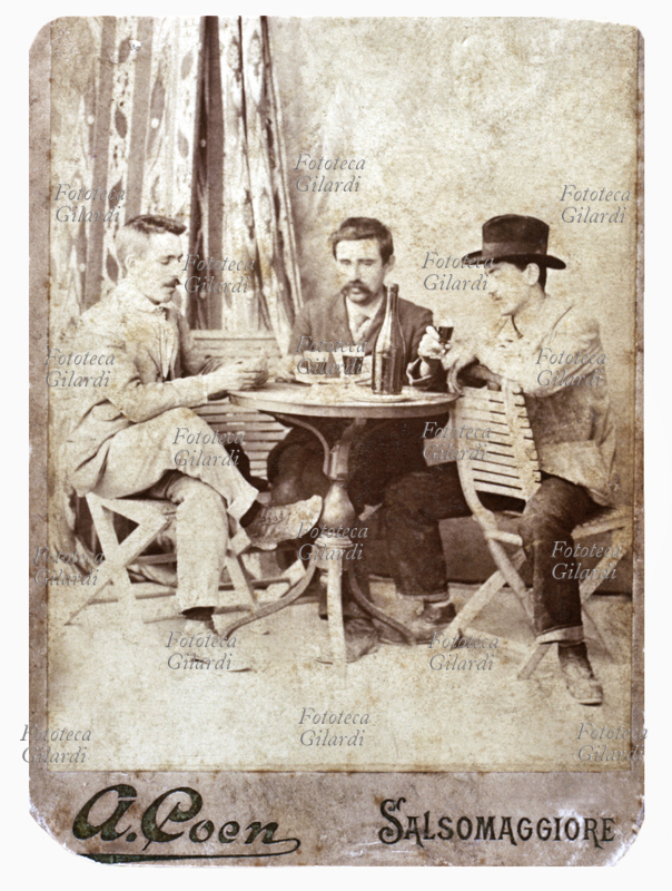 VINO Due amici giocano a carte al tavolino, un terzo li osserva bevendo del buon vino. (A. Coen, Salsomaggiore) Italia, 1903 circa