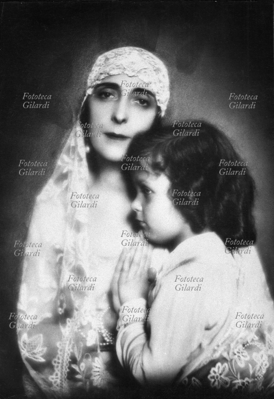 Ghitta CARELL (20 settembre 1899 – 18 gennaio 1972), ritratto di donna velata di bianco con infante; il piccolo, di profilo, avvolto nell\