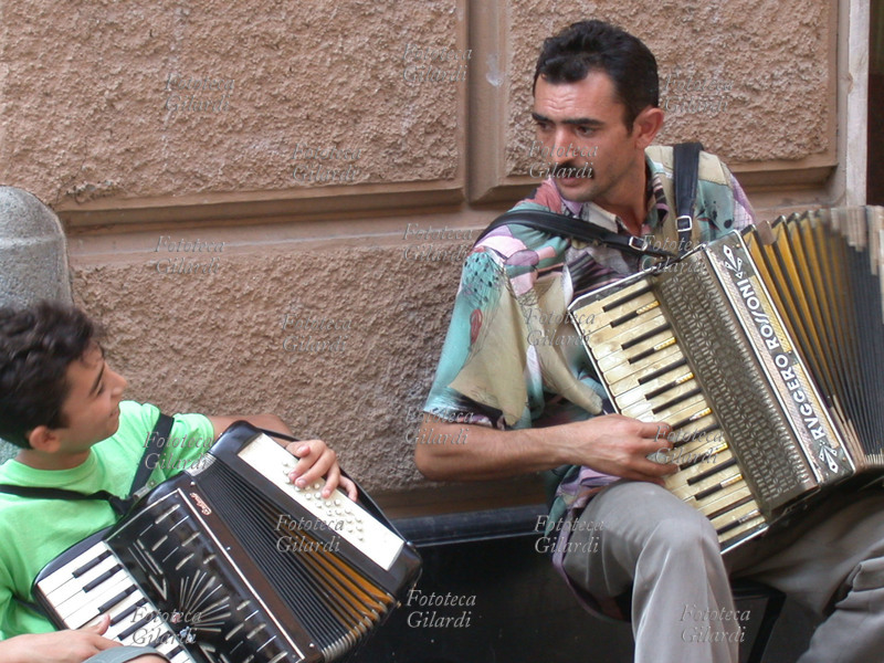 MUSICA Coppia di suonatori ambulanti di fisarmonica, ragazzo e adulto. Immagine orizzontale parte di una sequenza. Fotografia Giuliano Grasso, Rapallo (GE) 2002