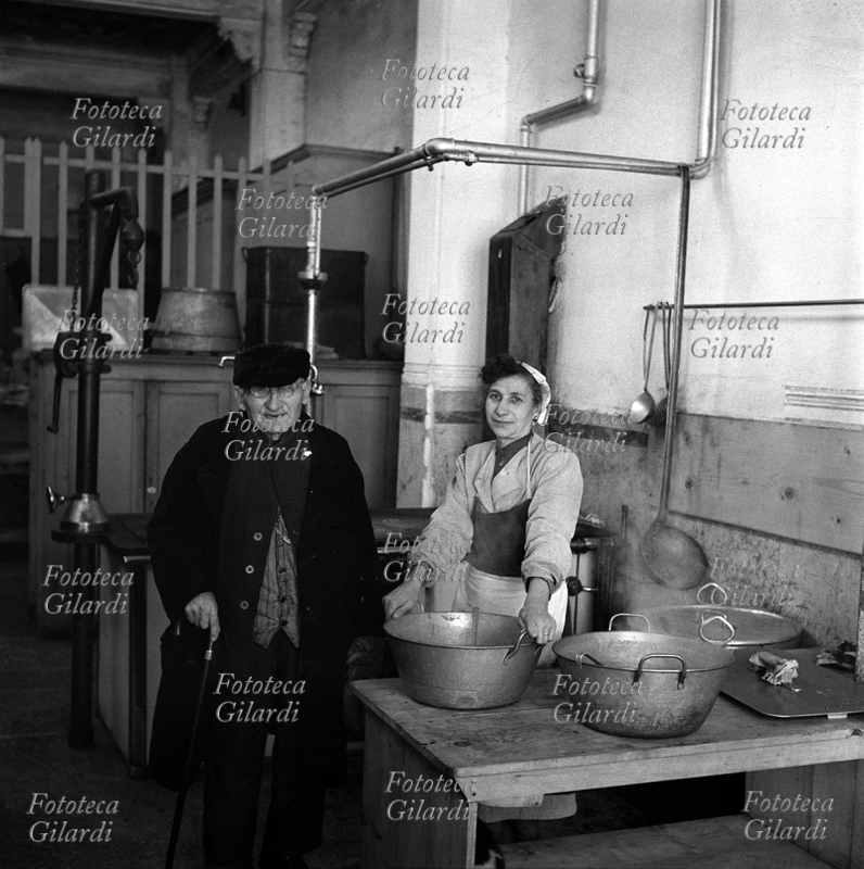 CUOCA di mensa operaia; nella cucina dello stabilimento Bruzzo, durante le lotte nelle fabbriche del genovese contro la smobilitazione ed i licenziamenti, un vecchio dipendente porta la solidarietà ai lavoratori. Fotografia di Ando Gilardi (1921-2012) #andogilardi, Genova 1952.