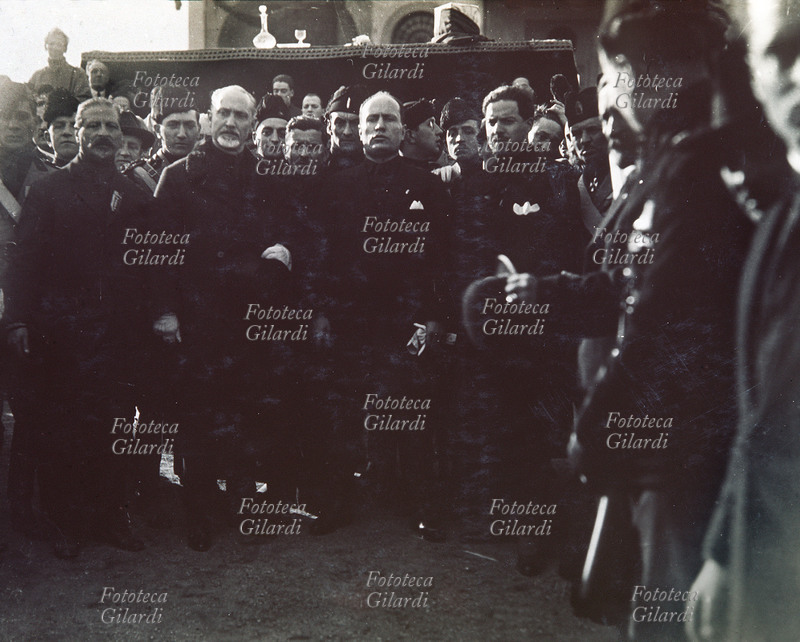 Benito MUSSOLINI (29 luglio 1883 – 28 aprile 1945) in camicia nera durante una commemorazione della marcia su Roma; tra gli altri, nel gruppo, Italo Balbo (6 giugno 1896 – 28 giugno 1940). Italia, 1926 circa.