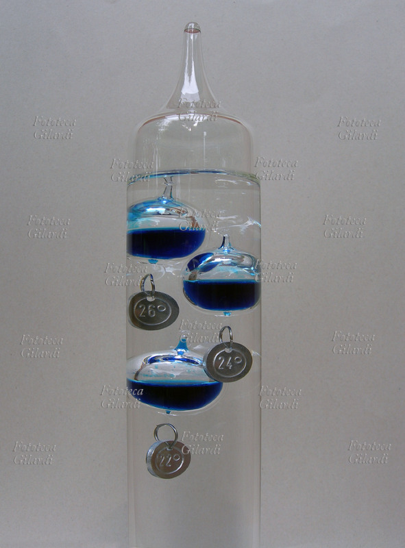TERMOMETRO galileiano. Dettaglio delle tre sfere dei gradi 26, 24, 22. Il termometro è un tubo di vetro saldato riempito con acqua in cui sono immerse alcune ampolle di vetro riempite con una miscela liquida colorata (alcol o acqua con colorante). Ogni ampolla ha attaccata una leggera targhetta metallica che indica numericamente una temperatura. Il peso di ciascuna targhetta è accuratamente calibrato e differente l\