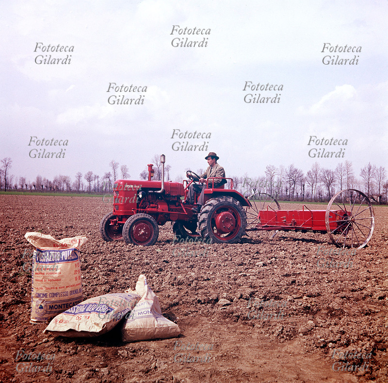 AGRICOLTURA Un agricoltore sparge col trattore sul terreno arato una miscela fertilizzante di \