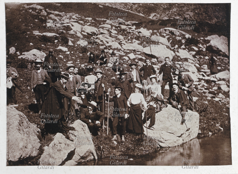 MONTAGNA esteso gruppo misto di ventitre turisti, in posa durante la pausa di una escursione in montagna, nei pressi di un laghetto; il burlone della compagnia finge di volersi tuffare giungendo le mani verso l\