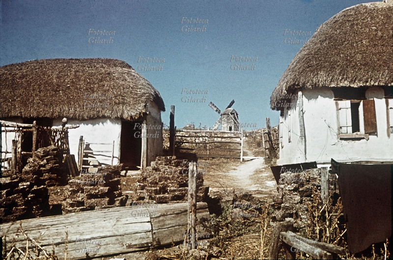 II G.M. URSS ITALIA Veduta di un villaggio attraversato dagli alpini in marcia. Tra le isbe si vede un mulino a vento. Rara testimonianza fotografica a colori di Gianfranco Ucelli (Battaglione Aquila, 3° Art. Alpini.), uno tra i pochi reduci sopravvissuti alla tragica spedizione in Russia. U.R.S.S. estate 1942.