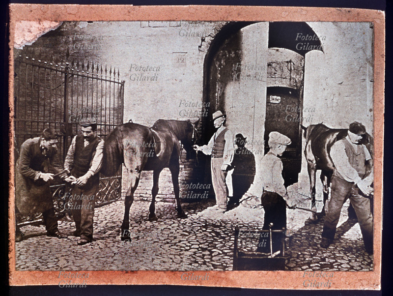 MESTIERI due maniscalchi ritratti mentre ferrano lo zoccolo del rispettivo cavallo. Italia, 1900 circa