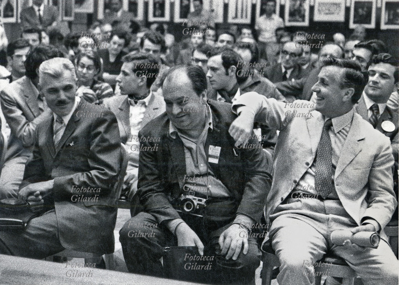 Ando GILARDI (1921-2012) e Lanfranco COLOMBO (1924-2015) tra il pubblico di una presentazione ad una mostra fotografica che si vede alle loro spalle. Non ci sono notizie più definite, si presume: Milano 1968 circa