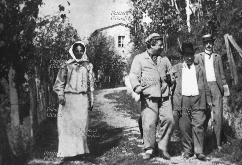 Giovanni PASCOLI (31 dicembre 1855 – 6 aprile 1912) il poeta seguito dalla sorella Mariù (Maria, 1º novembre 1865 – 5 dicembre 1953), biografa e conservatrice delle sue opere, conduce gli amici in giro per le vigne e gli oliveti della sua tenuta a Barga, frazione di Castelvecchio (Lucca). Dietro a loro si vede la casa. Fotografia, Italia XX secolo.