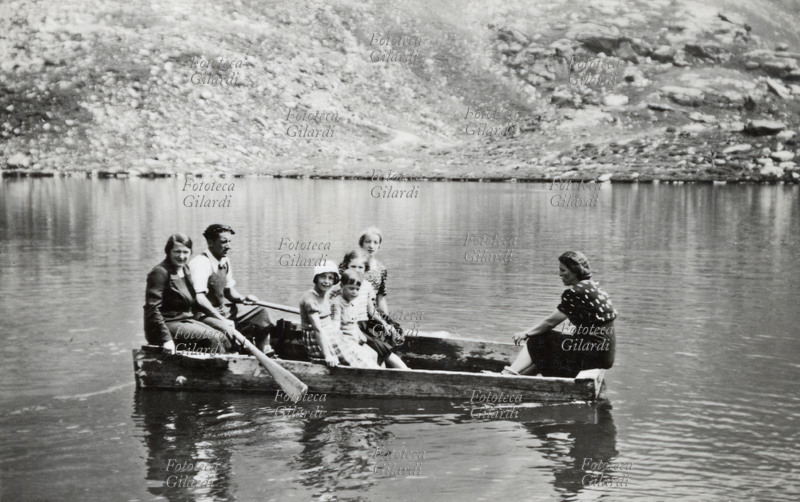 FAMIGLIA fotografia ricordo di una gita in barca sul lago; la piccola imbarcazione a remi ospita ben sette persone. Provincia di Lecco, Italia 1930 circa