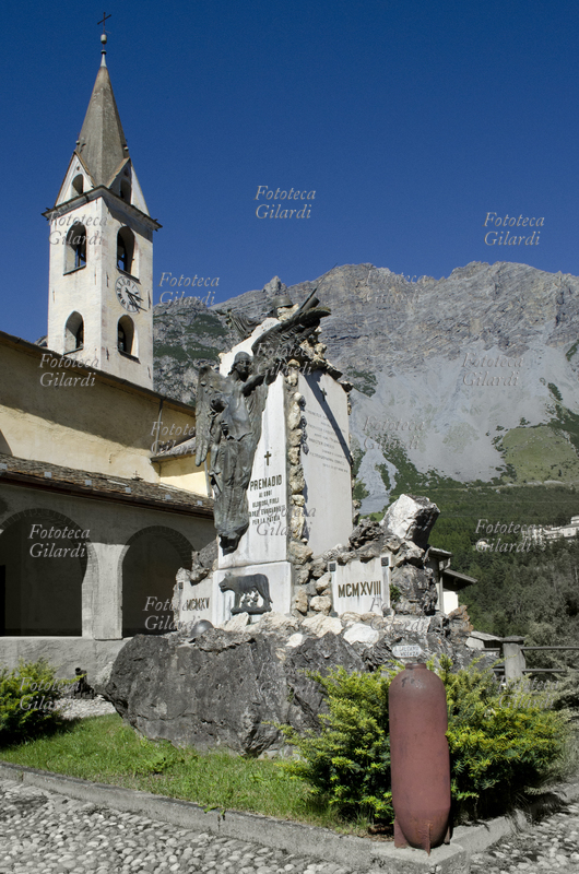 ITALIA 1915 - 1918 monumento commemorativo dedicato ai caduti della prima guerra mondiale dalla cittadinanza di Premadio, frazione di Valdidentro, Contea di Bormio (SO). In primo piano una bomba, residuato bellico, è usata come elemento decorativo; sullo sfondo, le Alpi e la chiesa. Fotografia di Elena Piccini, Italia, 2016