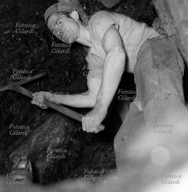 MINIERA minatore al lavoro con piccone nella antichissima miniera di lignite a Luni, detta la Lunara, da cui si estraeva già al tempo degli Etruschi. La lignite è un carbone fossile con caratteristiche di combustibile poco pregiate, entrato in disuso nel secondo dopoguerra (1950-60). Gli operai occuparono questa miniera nel tentativo di impedirne la chiusura, che poi invece avvenne con conseguente licenziamento dei lavoratori. Fotografia di Ando Gilardi (1921-2012) #andogilardi, eseguita con illuminazione di bulbi al magnesio. Luni (La Spezia), 1953.