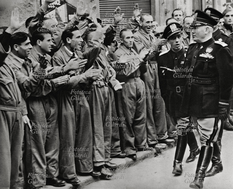 FASCISMO Mussolini in visita agli operai che rispondono festosi con il saluto romano. Fotografia di propaganda del regime, 1936 circa.