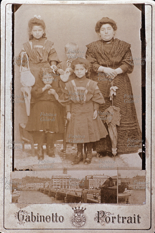 FAMIGLIA madre in posa con i suoi quattro figli: tre femmine, ancora bambine, e un maschio, il più giovane, che tiene in mano una chitarrina. Il ritratto è eseguito in atelier \