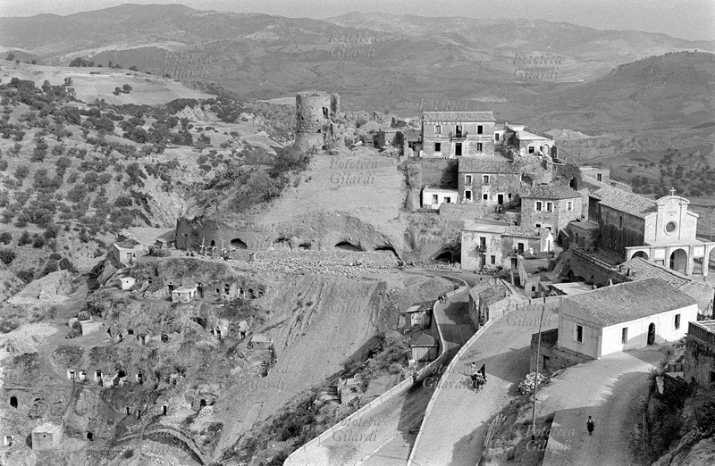 MELISSA Veduta del paese arroccato sulla collina, con le mura medievali e i ruderi del castello feudale; le abitazioni nella parte bassa sono singolarmente scavate nella pietra: caverne nella collina. Fotografia di Ando Gilardi (1921 - 2012) #andogilardi, Melissa (Crotone), 1954 circa.