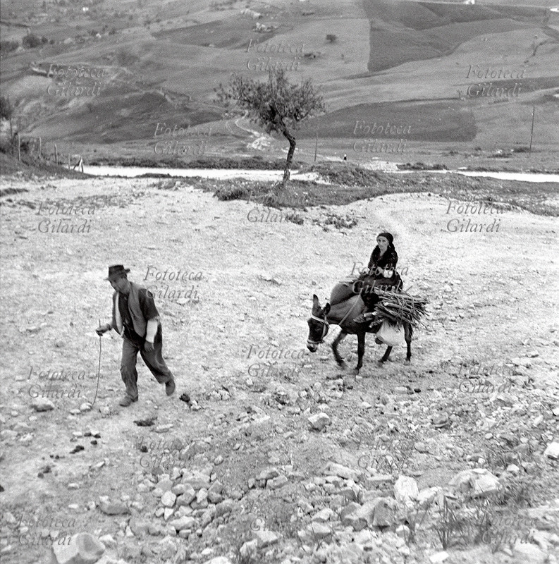 AGRICOLTURA coppia composta da un uomo ed una donna anziana al ritorno dai campi: lei cavalca un piccolo asino che porta sulla groppa anche due fascine di legna. L\