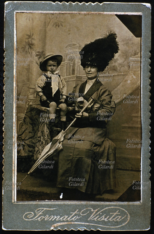 FAMIGLIA madre e figlio, elegantissimi, in posa dal fotografo davanti ad un fondale scenografico. Sono in abito \