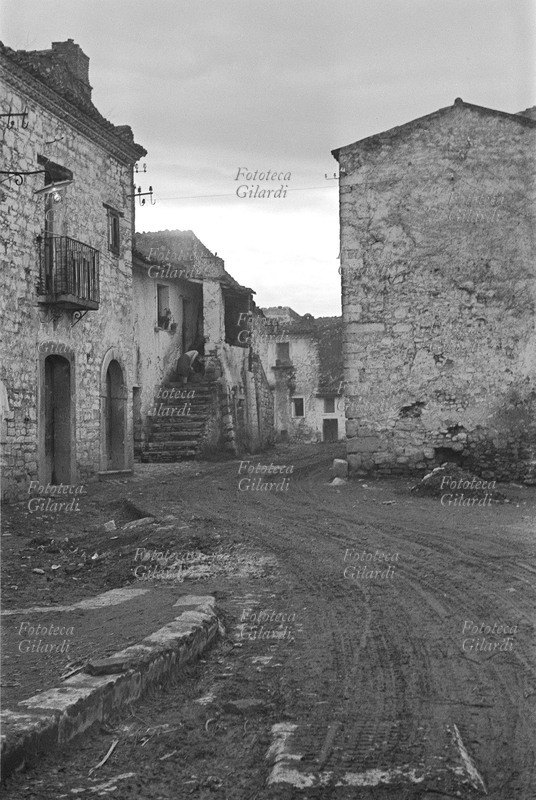 ITALIA S.M.O. Venosa, la strada fangosa tra le abitazioni è Via Roma; si notano i mucchi di fango ammassati dai manifestanti durante lo sciopero a rovescio. La rimozione del fango che aveva invaso le strade era lo scopo della mobilitazione organizzata dai braccianti disoccupati, per esortare le autorità ad impiegare la manodopera disponibile nei lavori necessari, con il doppio beneficio di diminuire la disoccupazione e migliorare la vivibilità del paese. Fotografia di Ando Gilardi (1921-2012) #andogilardi, parte di un ampio servizio realizzato per \